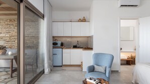 A compact living space with a kitchenette, a dining area, and a seating area with a chair and a coffee table. - Fos Suite by Vivian Horizon Tinos, Vivian Suites Tinos (Tinos)