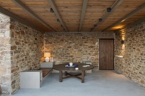 Una habitación con paredes de piedra y techo de madera, una mesa redonda con una bandeja azul, y una puerta.