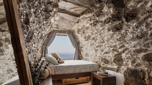 Ein Schlafzimmer mit Steinfassade, einem Bett mit Blick, einem kleinen Nachttisch und einem fenster mit Vorhängen.