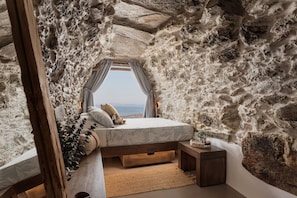 Un dormitorio con pared de piedra, cama con vistas, mesita de noche pequeña y ventana con cortinas.