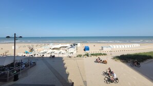 Blick auf einen Strand mit blauem Himmel, feinem Sand und einigen Personen sowie Fahrrädern.