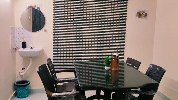 A small, private dining area with a black table, four chairs, a round mirror, a sink, and a trash bin. - Sarvik Thillai Residency  (Chidambaram)