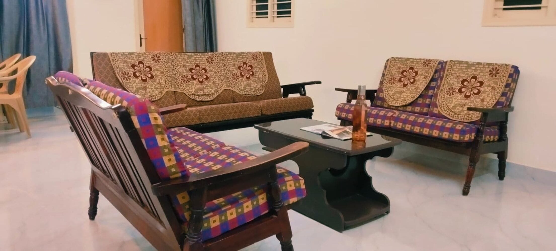 Una sala de estar con dos sofás, una mesa de centro, una silla de madera y una pequeña mesa con una botella.