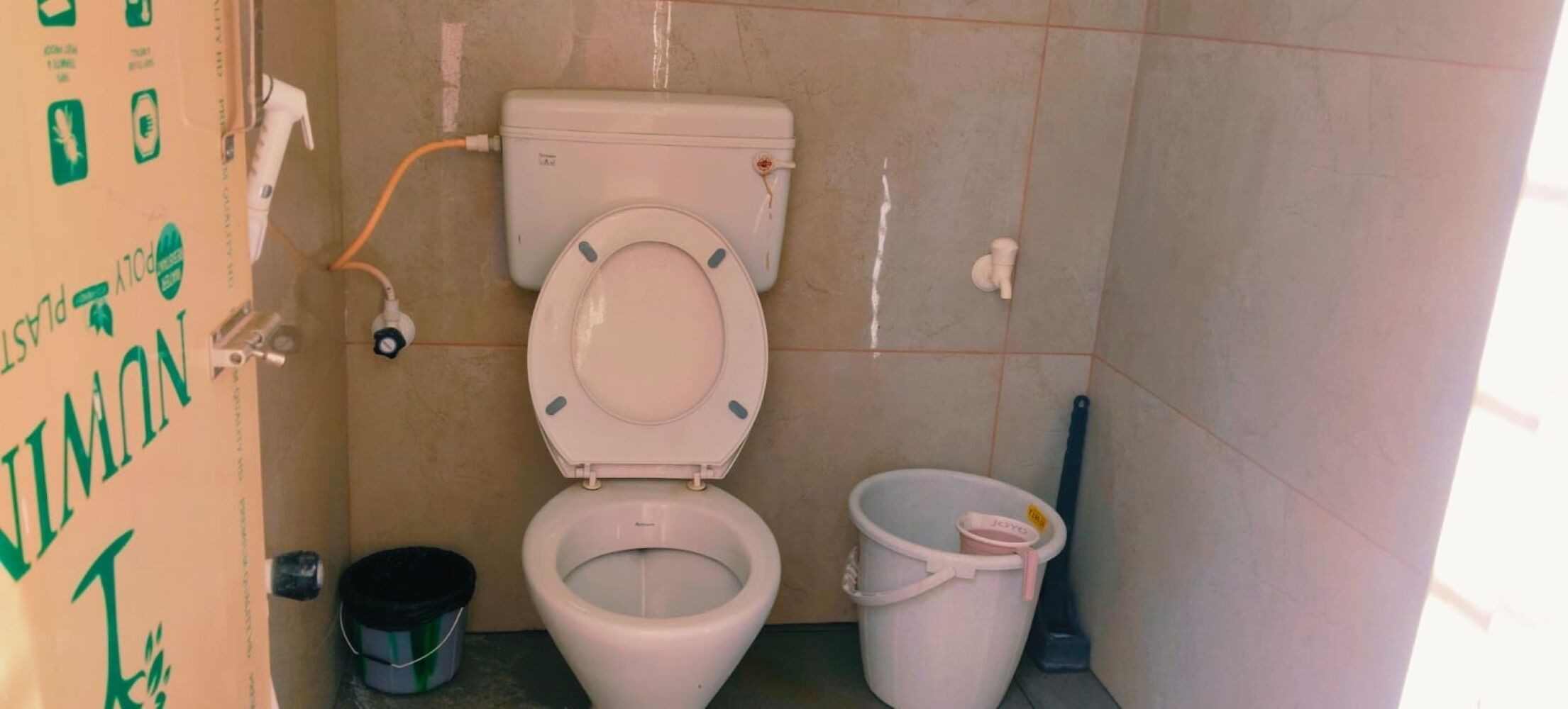 A bathroom with a toilet, a bucket, and a mop.