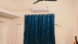 A bathroom with a white ceiling fan, a white air conditioning unit, a blue curtain with a leaf pattern, and a white door. - Sarvik Thillai Residency  (Chidambaram)