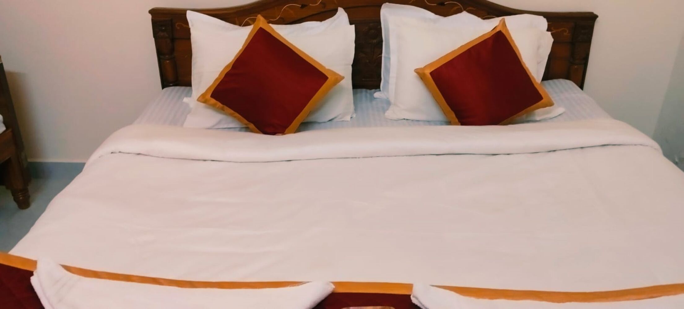 Una cama con cabecera de madera, ropa de cama blanca y dos almohadas rojas con adornos dorados.