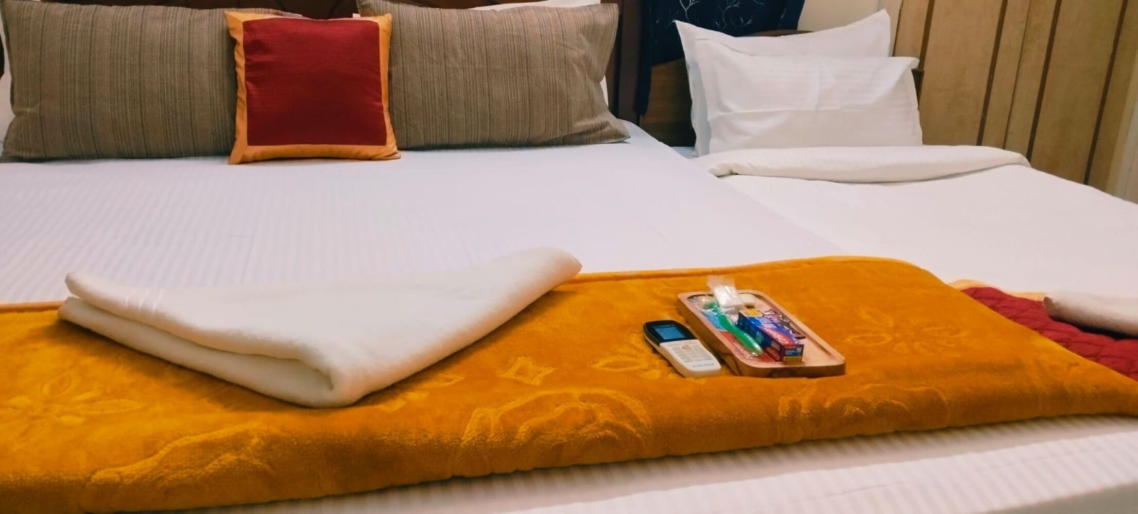 Un lit bien fait, avec une couverture blanche pliée, un oreiller rouge et un plateau contenant des articles de toilette.