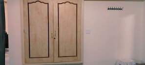 A room with a double wooden wardrobe, a coat rack, and a small table with a cloth.