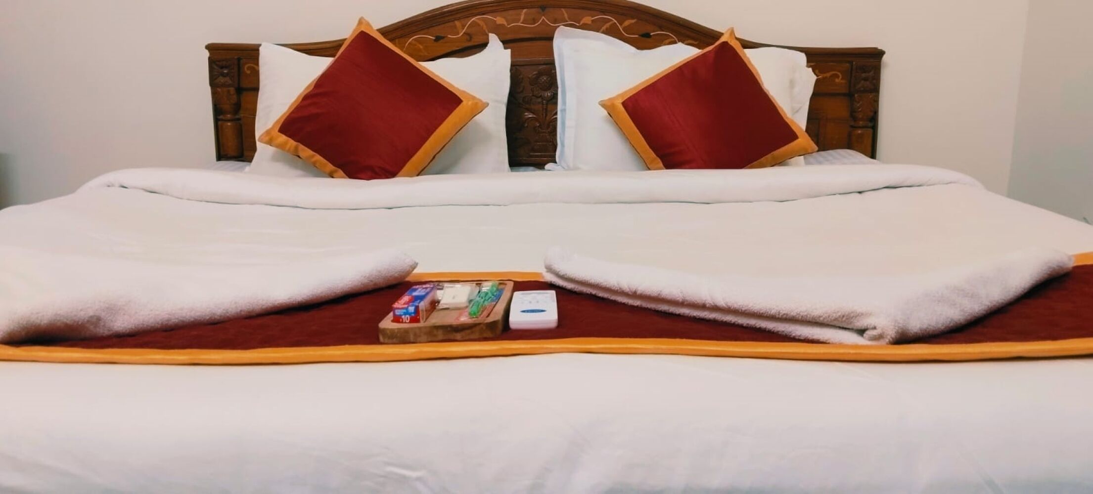 A neatly made bed with a wooden headboard, white bedding, and two red pillows.
