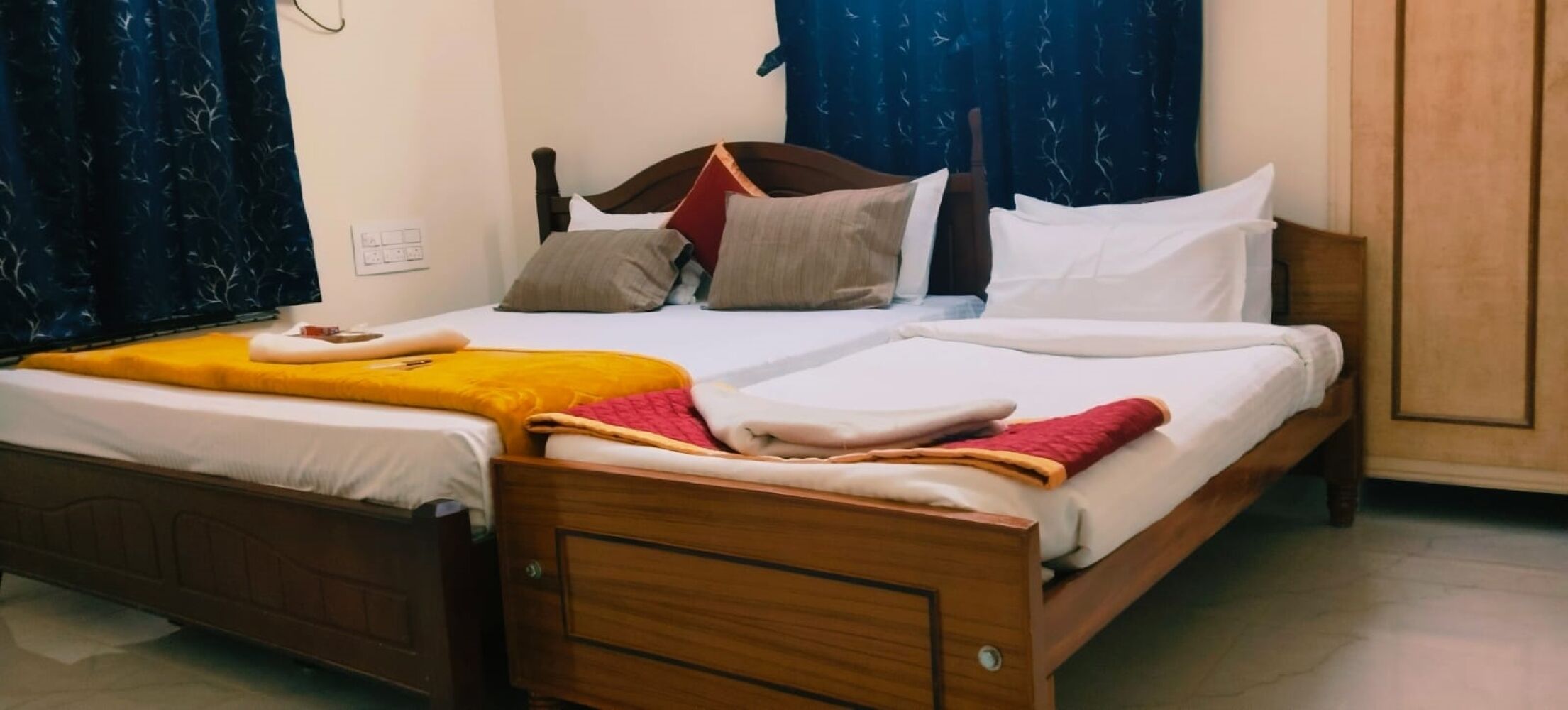Uma cama de casal com estrutura de madeira, duas almofadas, um cobertor amarelo e um xale vermelho.