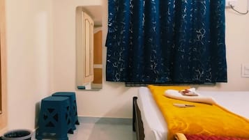 A bedroom with a bed, a small stool, a wardrobe, and a window with curtains.