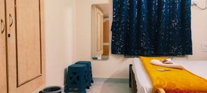 A bedroom with a bed, a small stool, a wardrobe, and a window with curtains.