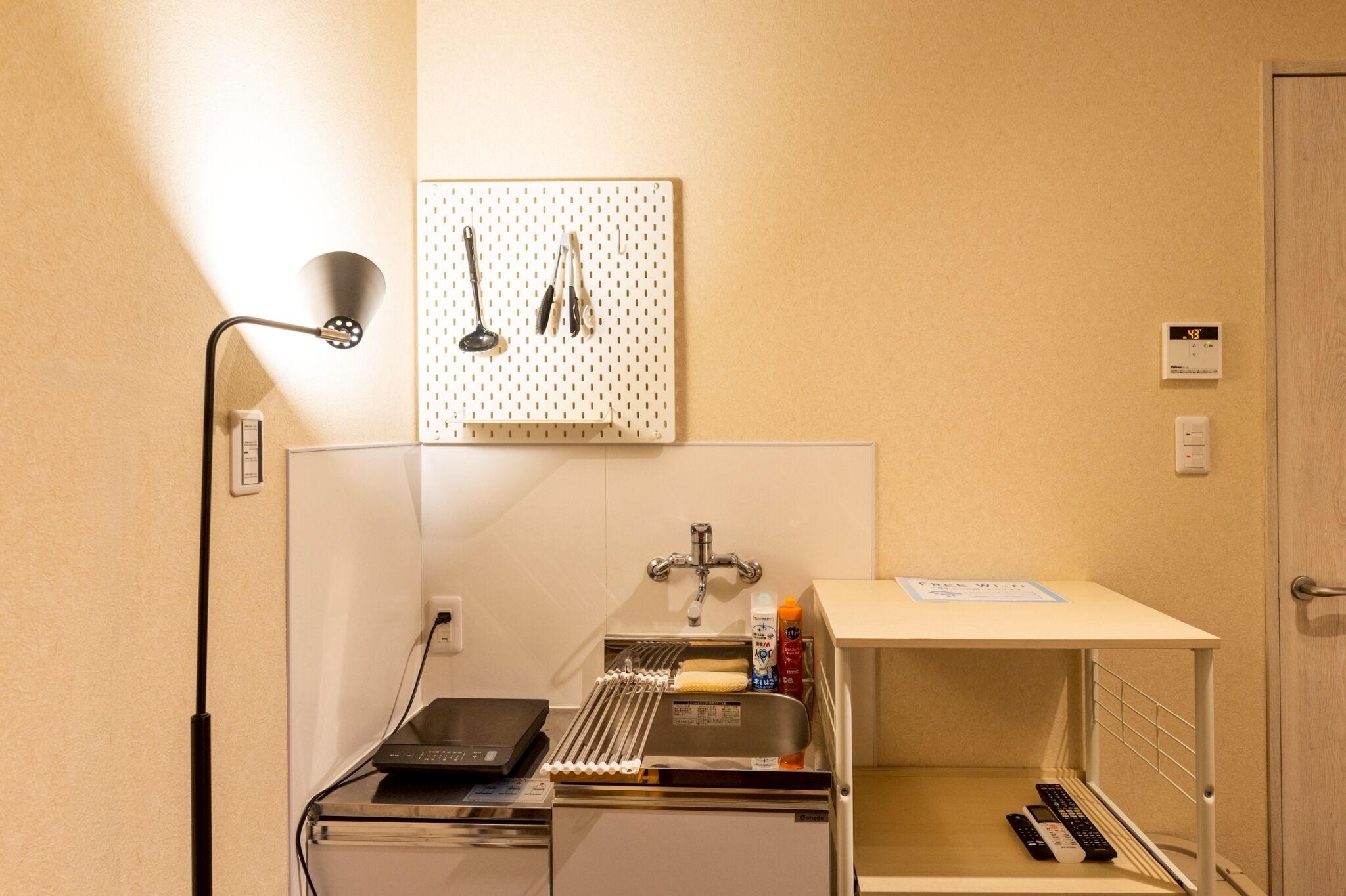 A compact kitchenette with a sink, a small countertop, and a wall-mounted pegboard with kitchen utensils.