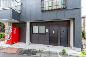 A building with a dark facade, a Coca-Cola vending machine, and a closed garage door. - Fukurouan (Toshimaku Kamiikebukuro)