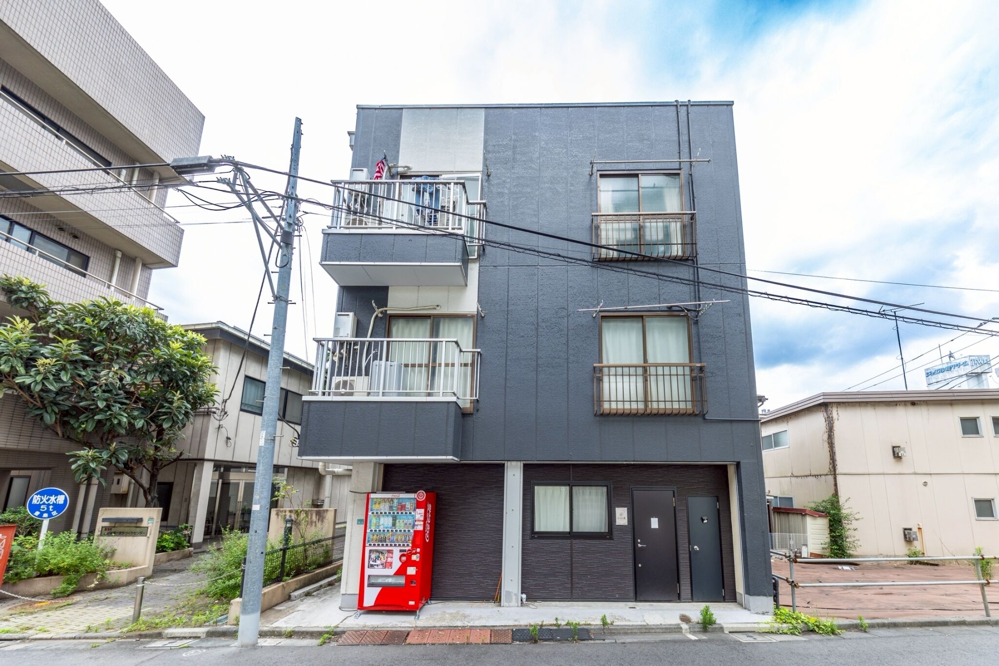 Um edifício com várias andares, varandas, uma máquina de vendas e uma porta.