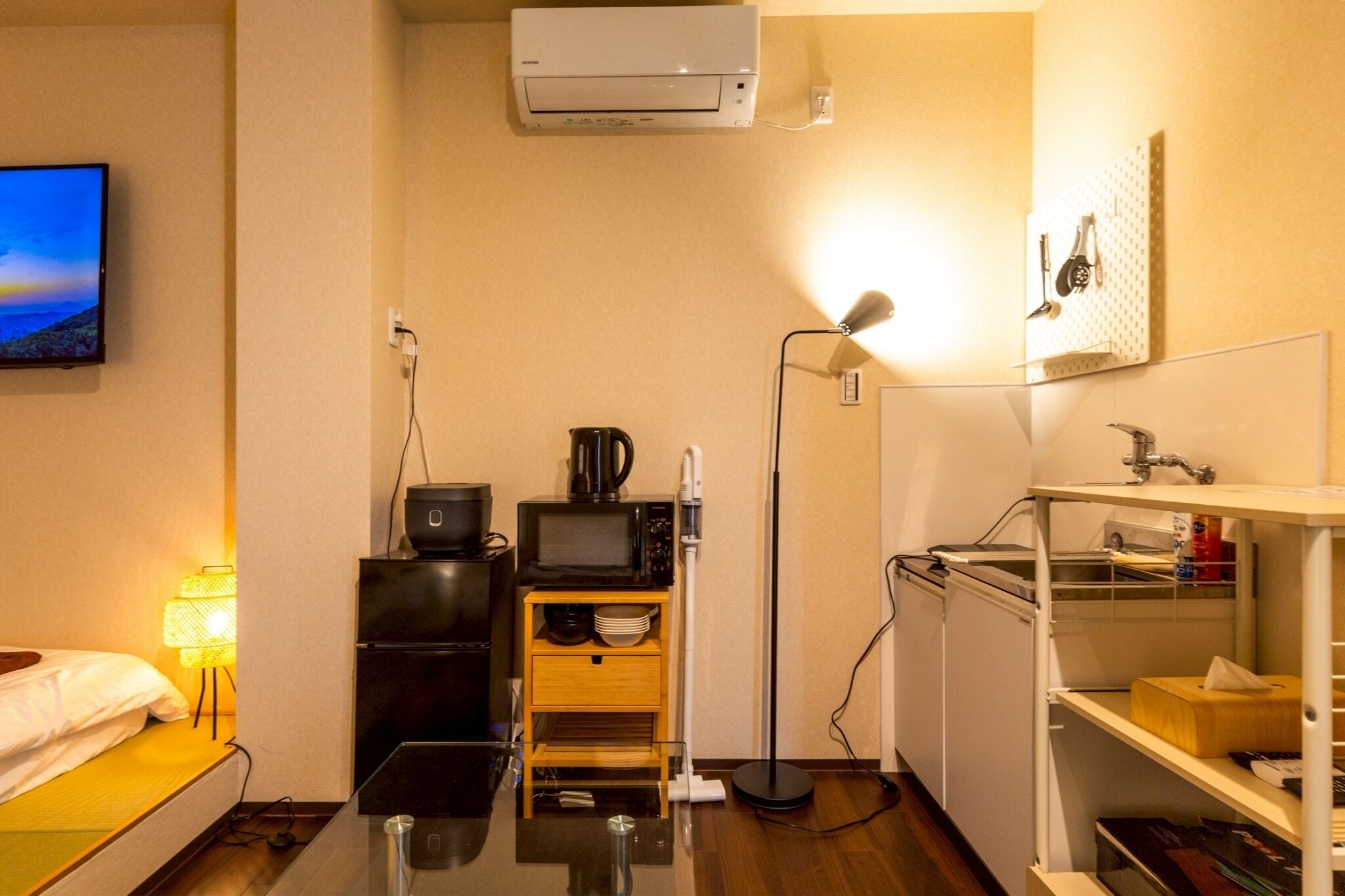 A compact hotel room with a bed, a TV, a kitchenette, and a small bathroom.