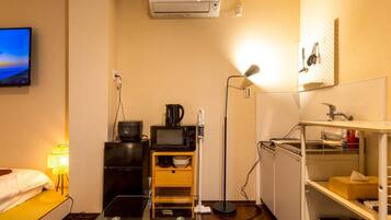 A compact hotel room with a bed, a TV, a kitchenette, and a small bathroom.