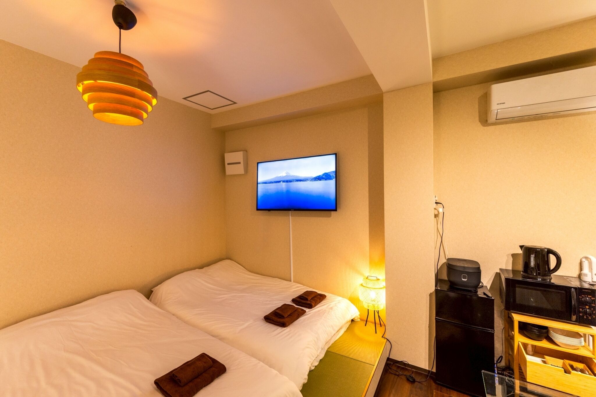 A hotel room with two beds, a television mounted on the wall, a coffee maker, and a microwave on a wooden shelf.