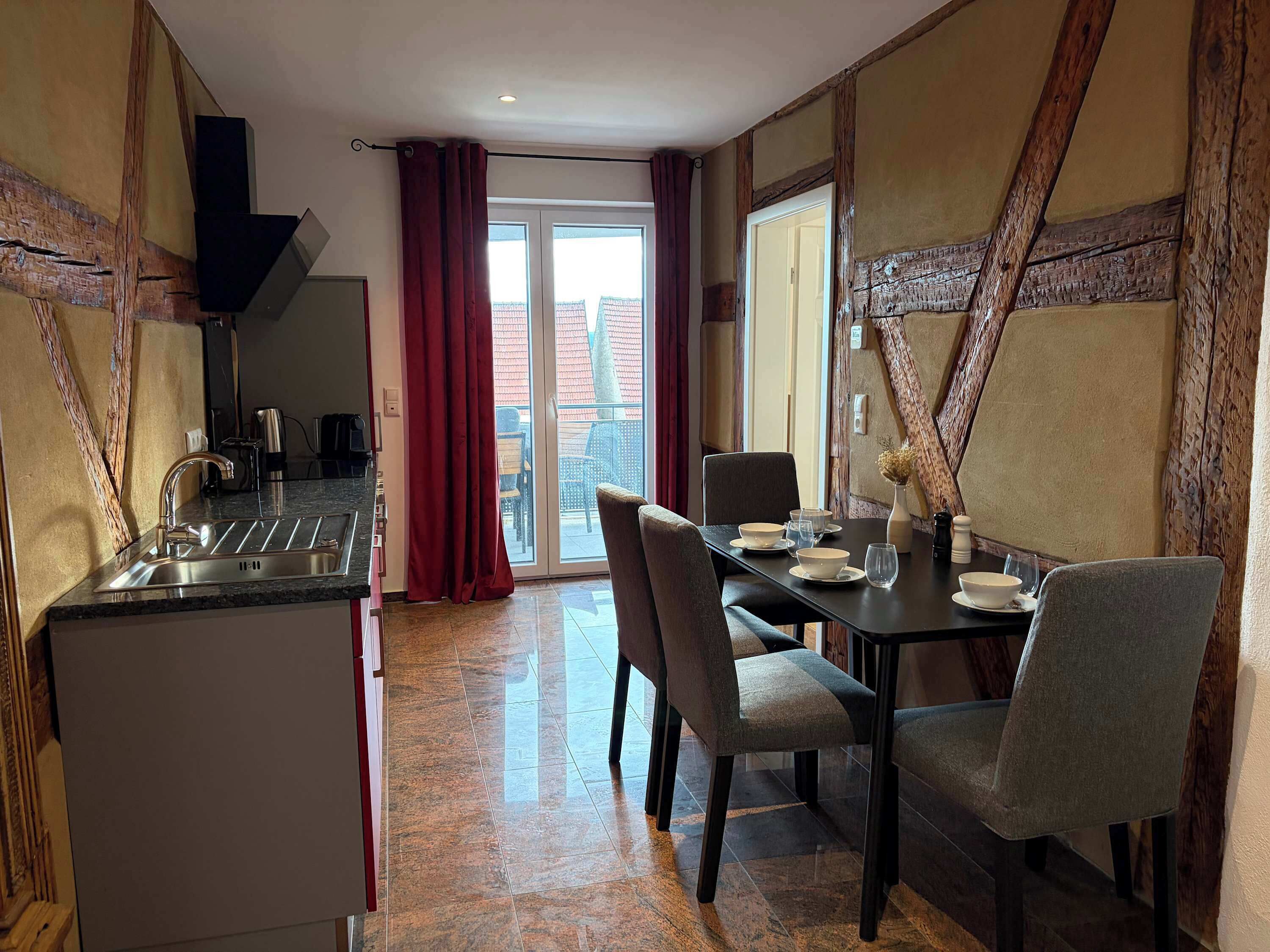 A dining area with a table set for two, a kitchen with a sink, and a sliding glass door leading to an outdoor balcony.