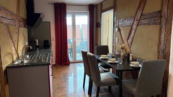 A dining area with a table set for two, a kitchen with a sink, and a sliding glass door leading to an outdoor balcony.