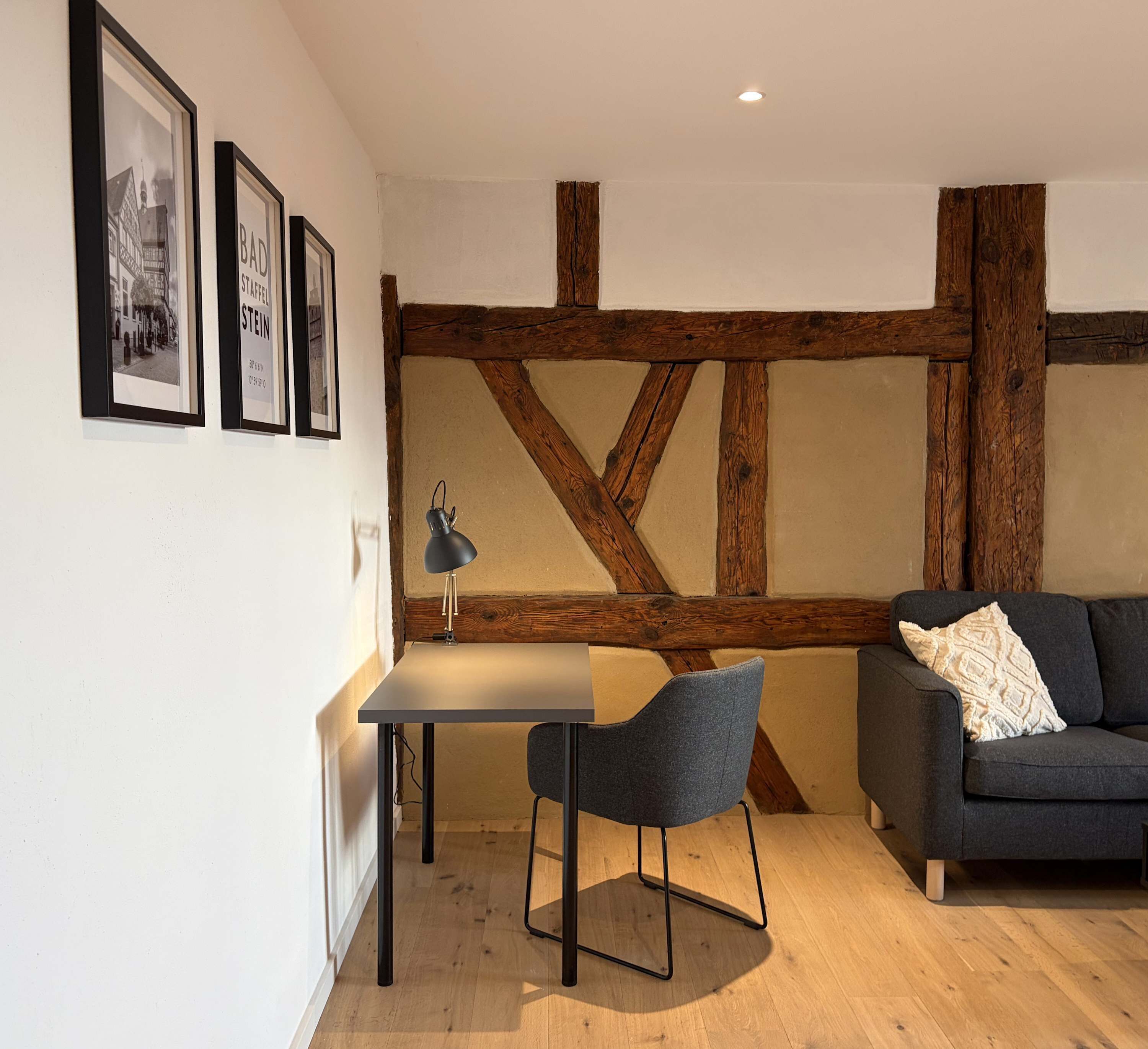 Una habitación con techo de vigas de madera, una mesa con una silla, un sofá y cuadros en la pared.