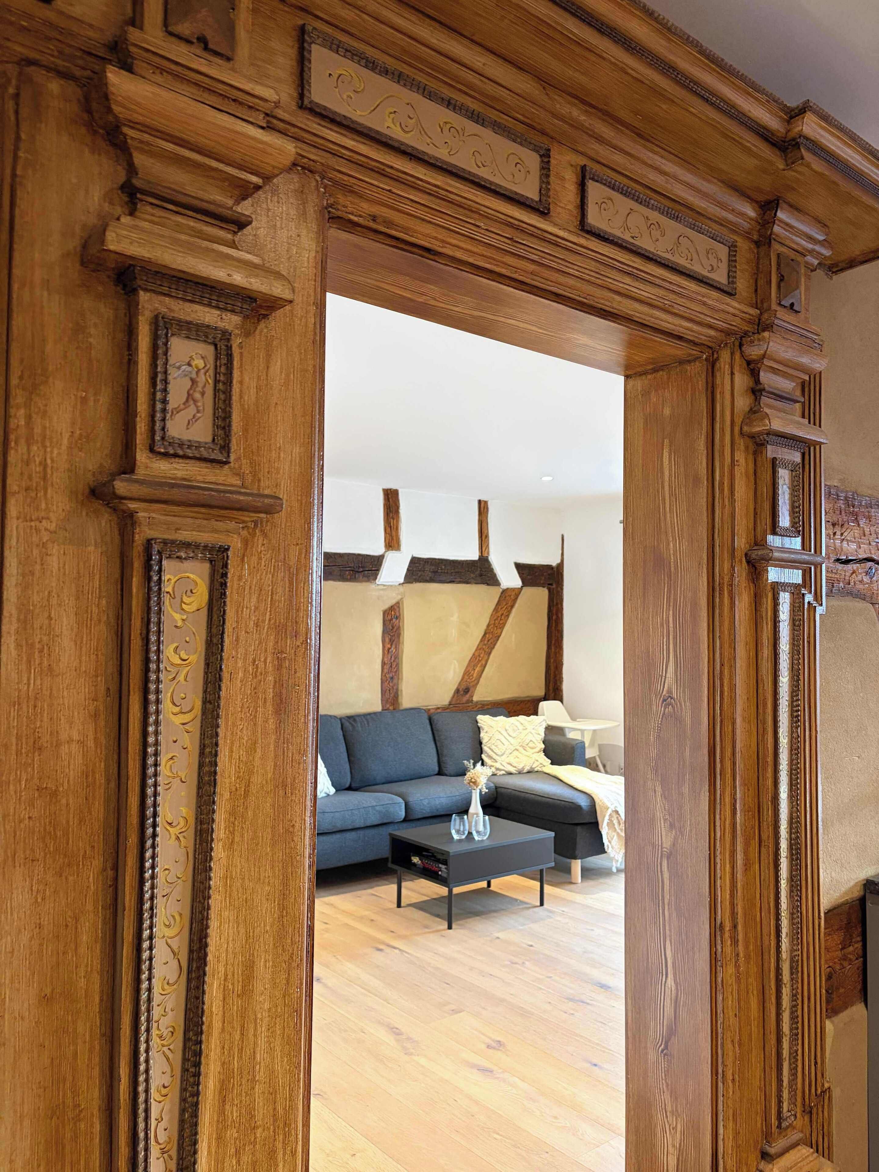 A wooden doorway leading to a living room with a sofa, a coffee table, and a fireplace.