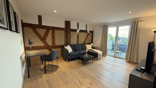 A modern living room with a sofa, coffee table, and a dining area with a table and chairs. - Juraperle - Historisch und modern - Wohnung 5 (Bad Staffelstein)