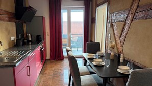 A modern kitchen with red cabinets, a dining area with a table set for two, and a view through a glass door to the outside. - Juraperle - Historisch und modern - Wohnung 5 (Bad Staffelstein)