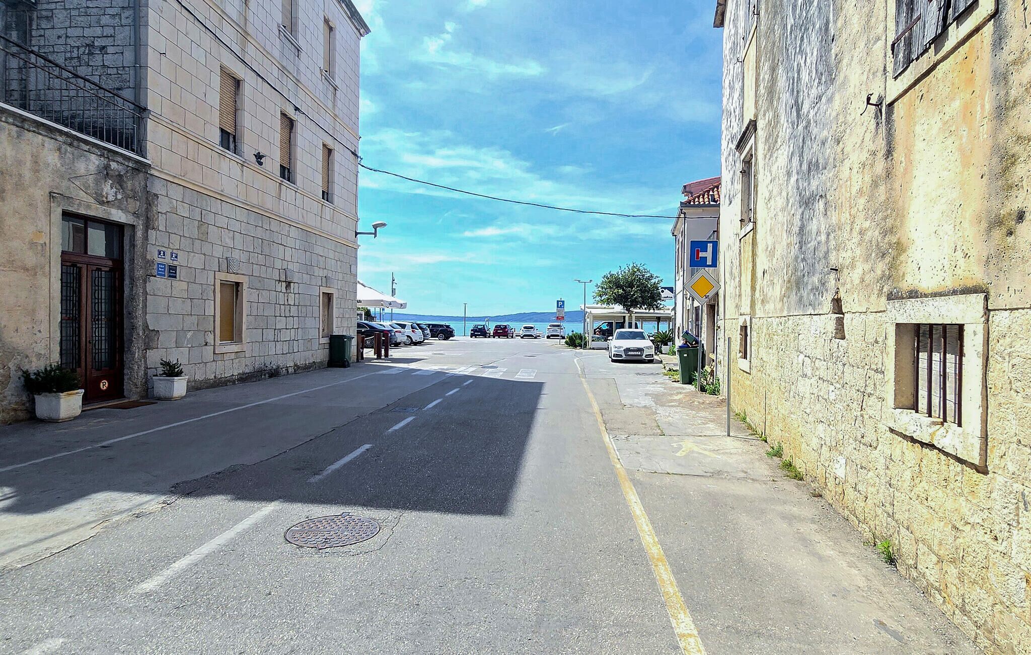 A narrow street with parked cars and buildings on either side.
