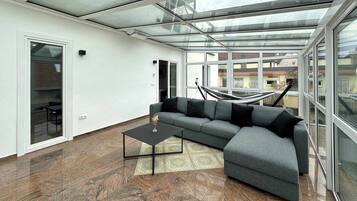 Ein modernes Wohnzimmer mit Glasdecke, einem grauen Ecksofa, einem schwarzen Couchtisch und einem gemusterten Teppich.