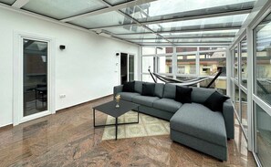A modern living room with a glass ceiling, a grey sectional sofa, a black coffee table, and a patterned rug. - Juraperle - Historisch und modern - Wohnung 3 (Bad Staffelstein)