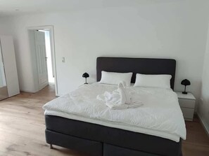 A neatly made bed with white linens and a folded towel, a bedside lamp, and a nightstand. - Juraperle - Historisch und modern - Wohnung 3 (Bad Staffelstein)