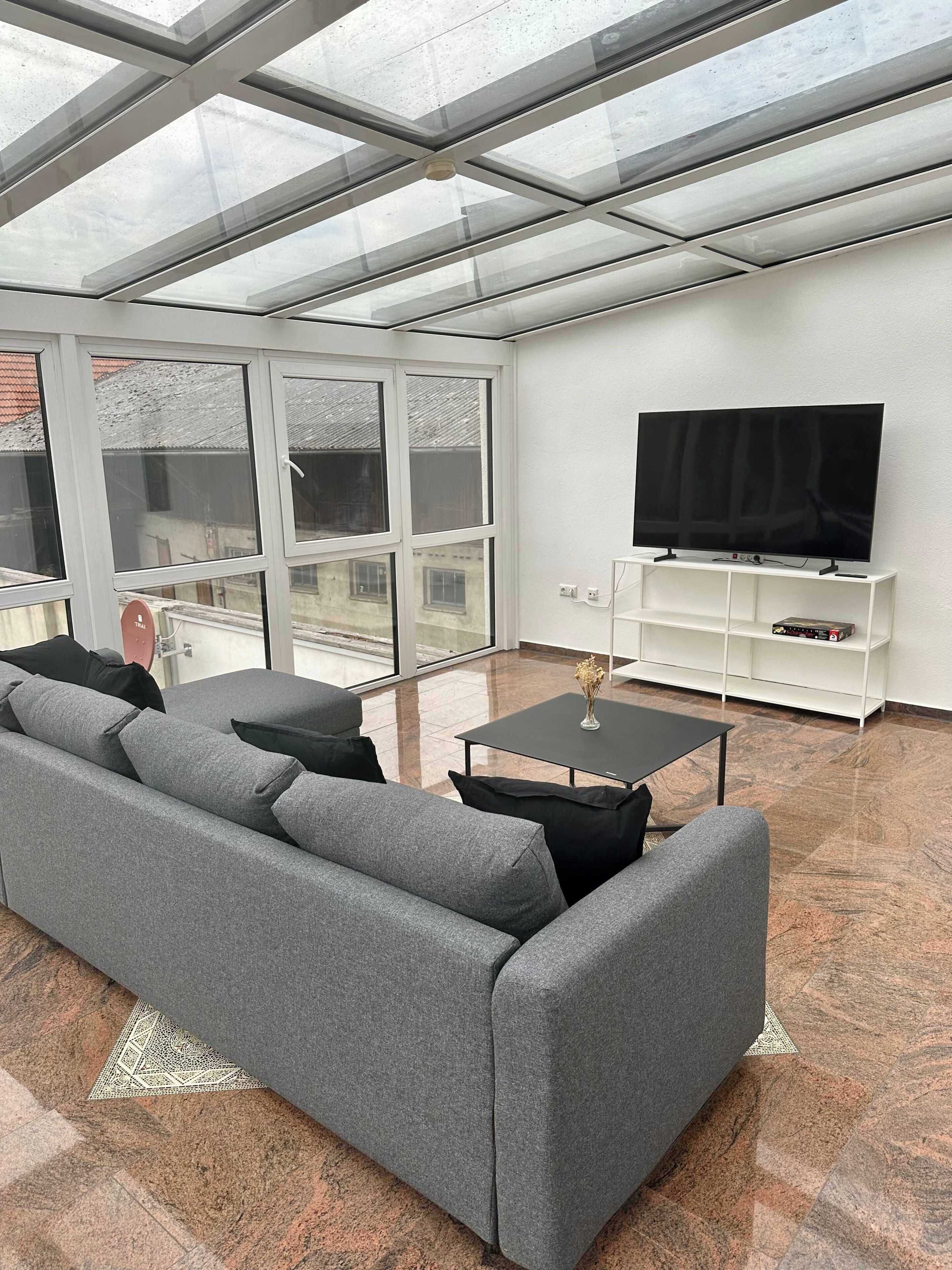 A modern living room with a grey sofa, a black coffee table, and a flat-screen TV on a white stand.