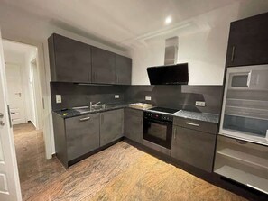 A modern kitchen with dark cabinetry, a built-in oven, and a microwave. - Juraperle - Historisch und modern - Wohnung 3 (Bad Staffelstein)