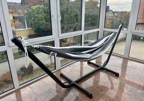 Una cadira de relax amb una etiqueta que indica el pes màxim suportat, situada davant d'una finestra gran que ofereix vistes a cases i arbres.