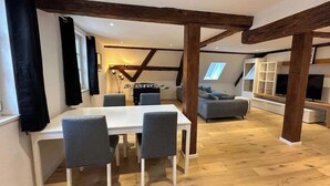 Un coin repas avec une table blanche et quatre chaises, un canapé et un téléviseur en arrière-plan.