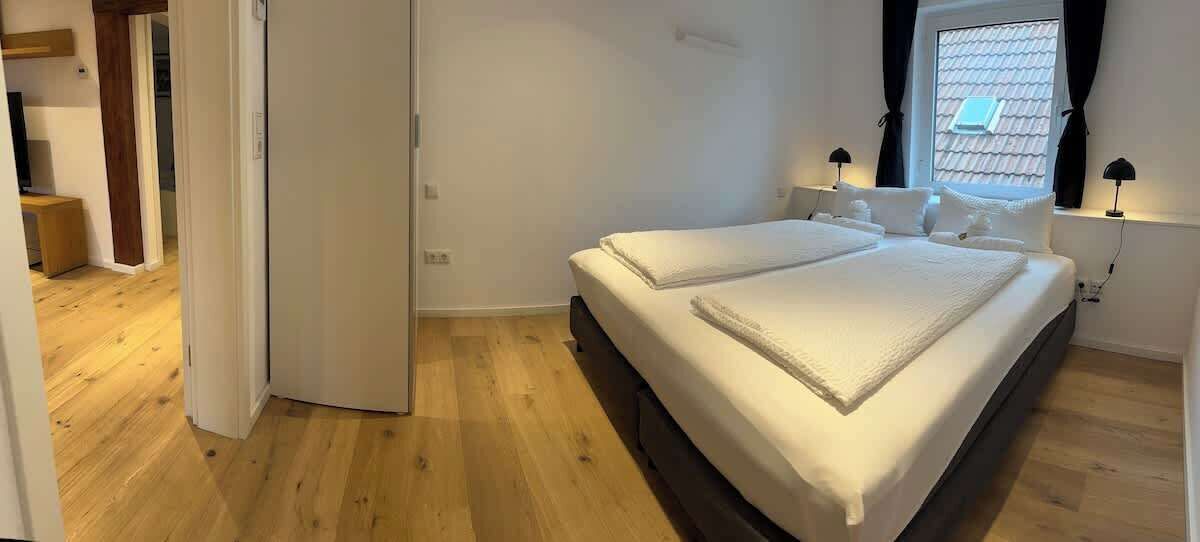 Une chambre avec un lit double, une fenêtre avec des rideaux et un plancher en bois.