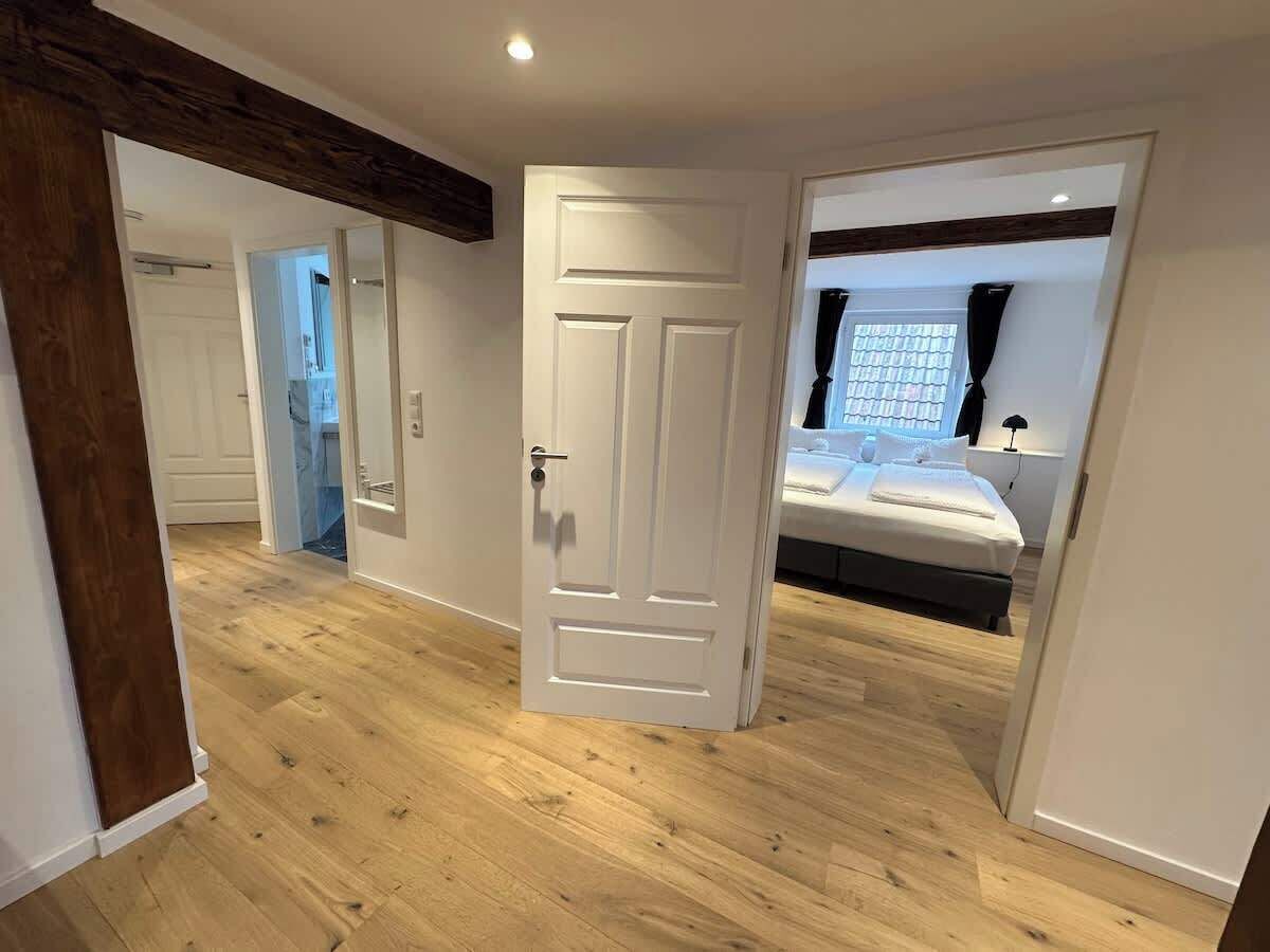 Ein Zimmer mit Holzboden, einer weißen Tür und einem Bett mit weißer Bettdecke.