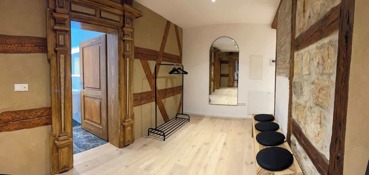 A room with a wooden door, a mirror, and a black shelf with shoes.