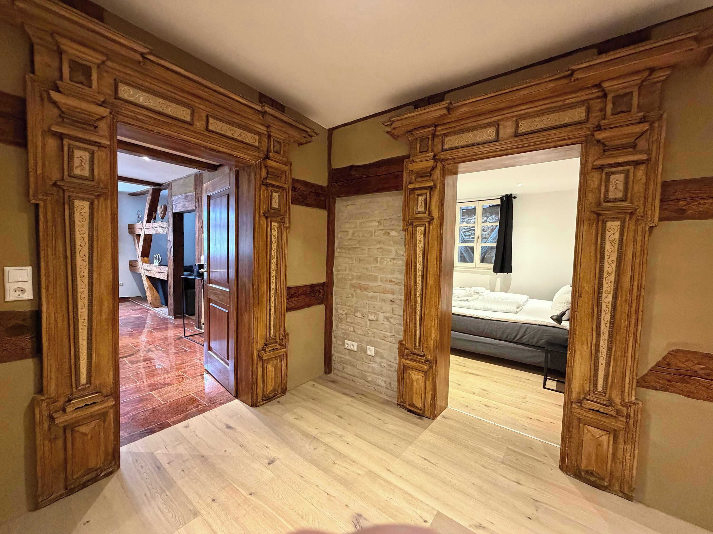 Ein Flur mit Holztürrahmen, der zu einem Schlafzimmer mit Bett und Fenster führt.
