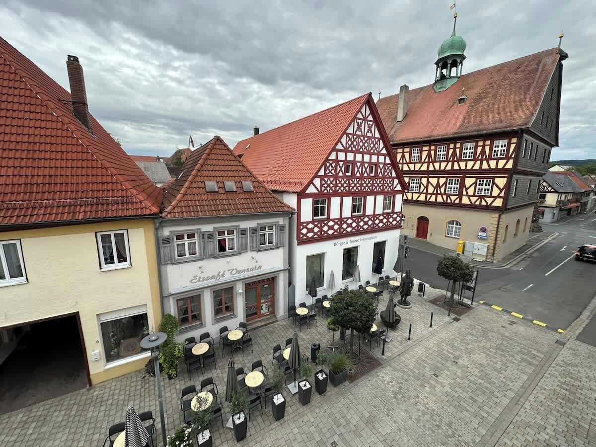 A traditional European town with half-timbered buildings, outdoor seating, and a cobblestone street.