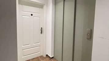 A hallway with a white door and a sliding glass door leading to a room. The floor is covered with brown patterned tiles.
