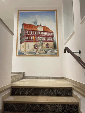Una escalera con acabado de mármol que conduce a una habitación con un cuadro grande de un edificio.