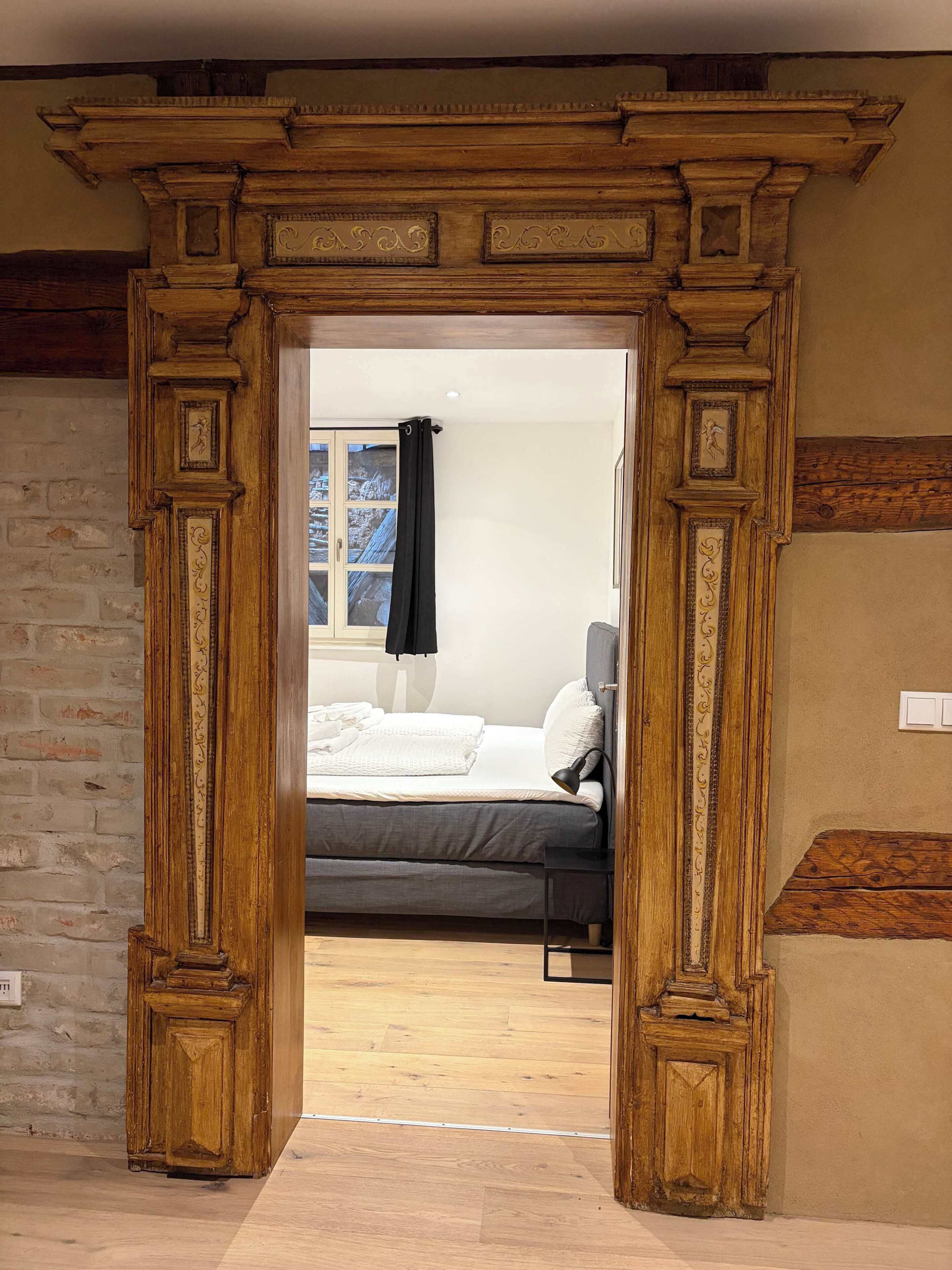 A doorway leading to a bedroom with a bed, a nightstand, and a window with a curtain.