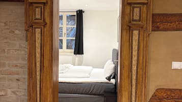 A doorway leading to a bedroom with a bed, a nightstand, and a window with a curtain.