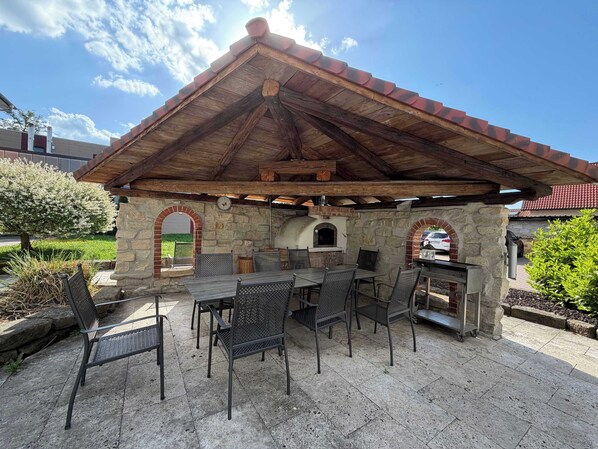 An outdoor patio with stone walls, a wooden roof, and a grill station.