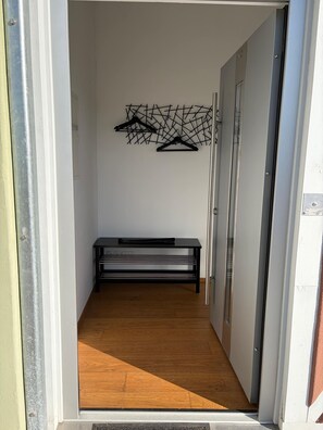 A hallway with a bench, a coat rack with multiple hangers, and a door on the right.