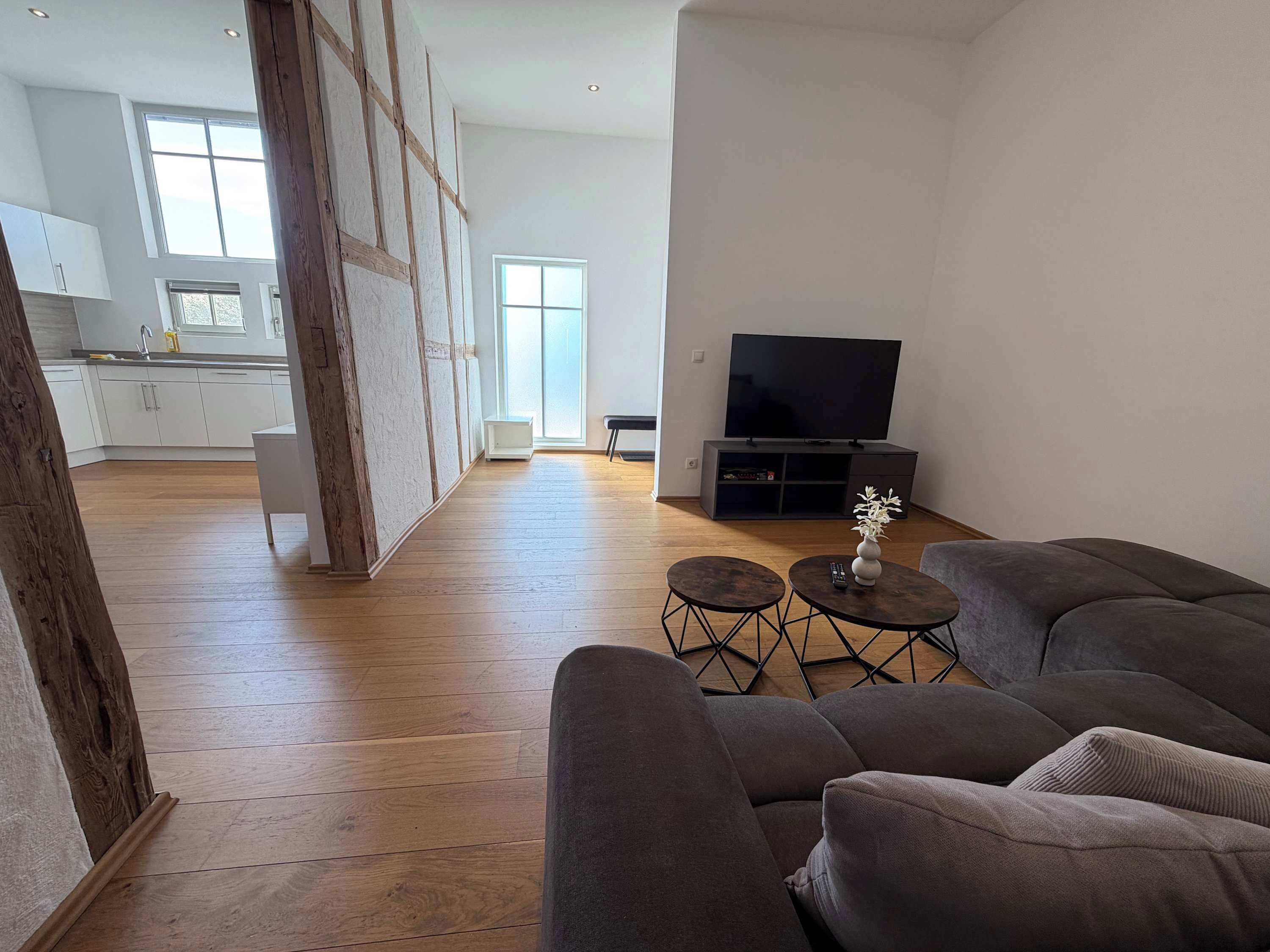 Ein modernes Wohnzimmer mit einem großen grauen Sofa, einem Flachbildfernseher und einem kleinen Tisch mit einer Vase.