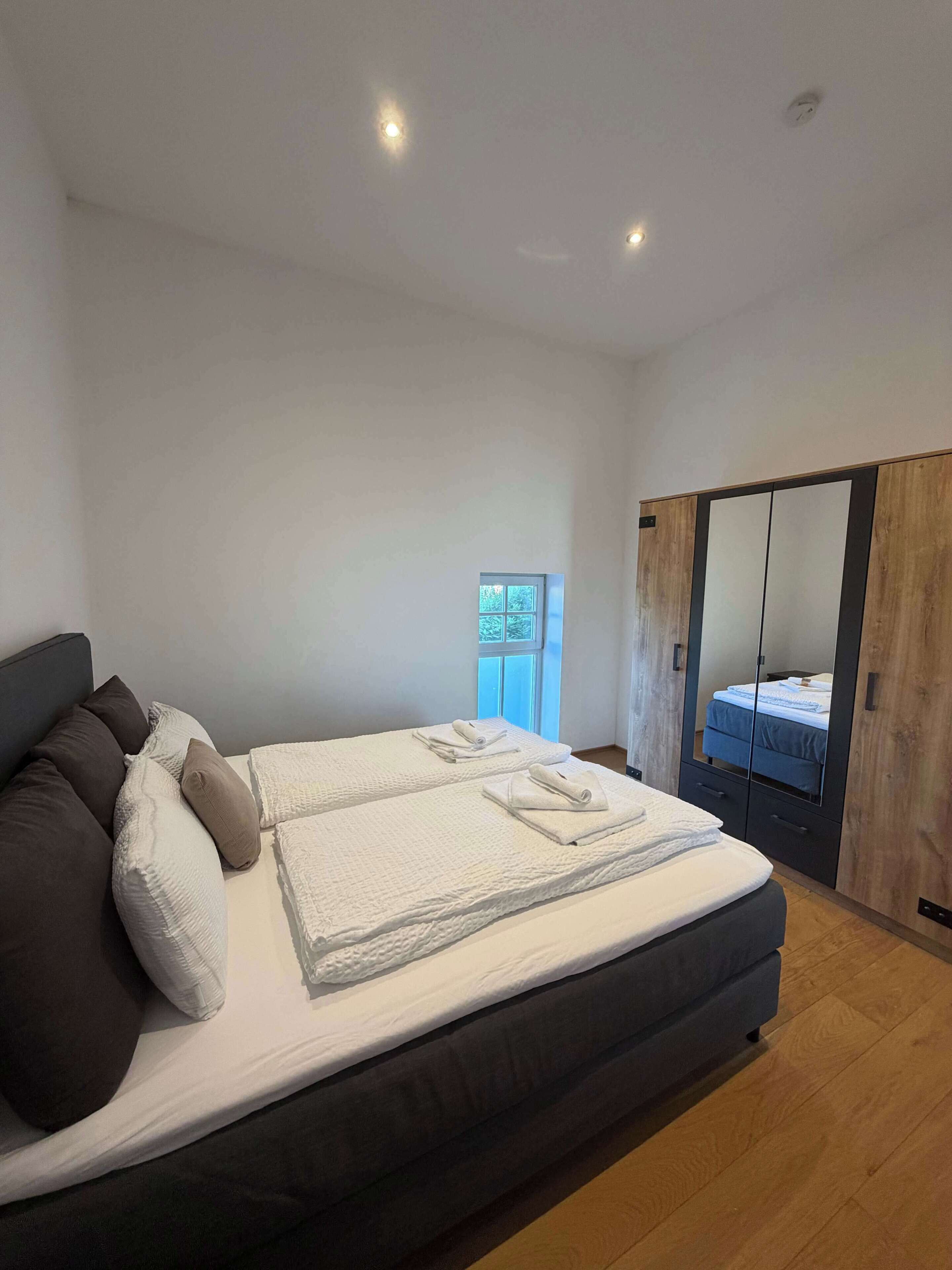 Een moderne slaapkamer met een groot bed, een inloopkast met spiegel en een klein raam.