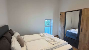 Een moderne slaapkamer met een groot bed, een inloopkast met spiegel en een klein raam.